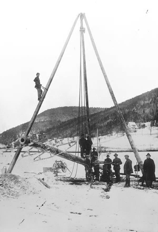 Historische Ansicht einer Strommast-Montage um 1910, ein Mann mit Gurt auf dem dreibeinigen Mast